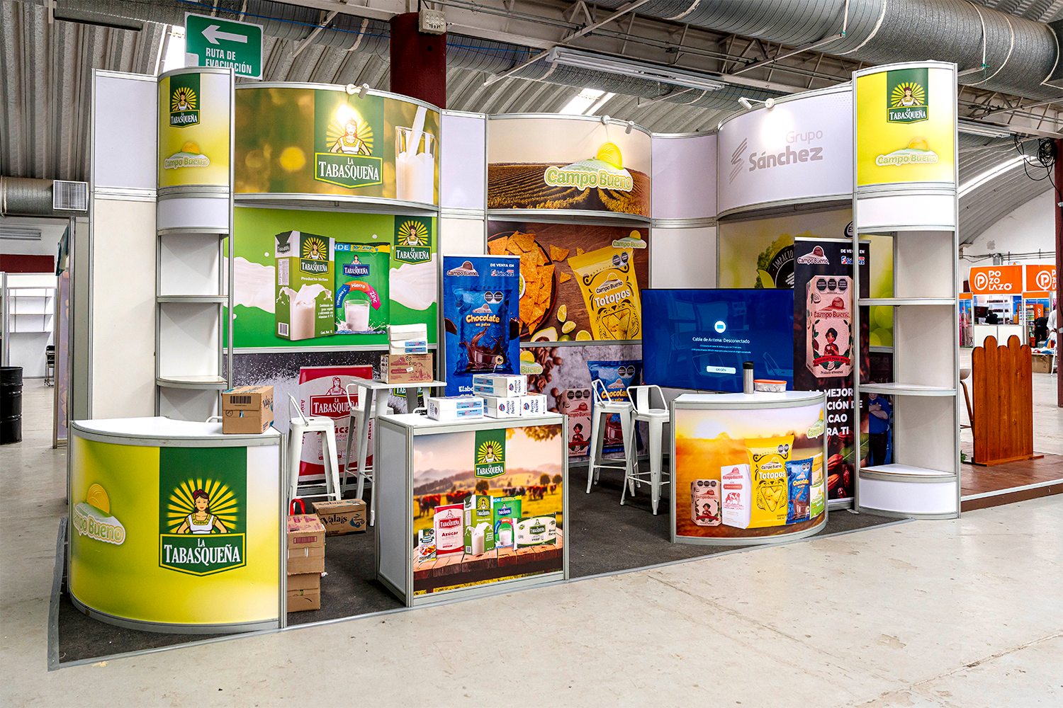 Gran stand curvo para la marca La Tabasqueña con múltiples mostradores y estantería.